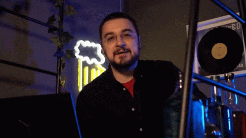 A Man With Glasses And A Beard Says " Scappa " In Front Of A Neon Sign GIF