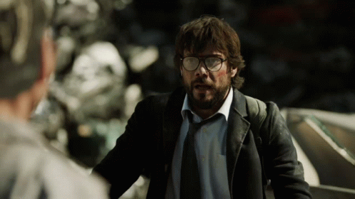 A Man With Glasses And A Beard Stands In Front Of A Pile Of Junk GIF