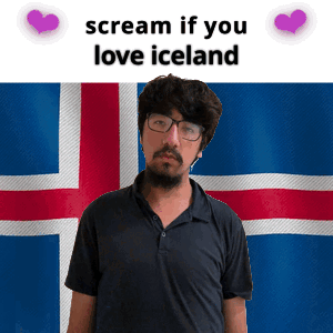 A Man With Glasses And A Beard Stands In Front Of An Iceland Flag GIF