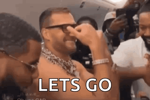 A Man With Glasses And A Chain Around His Neck Is Covering His Nose With His Hand And The Words `` Lets Go '' Are Visibl GIF