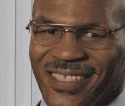 A Man With Glasses And A Mustache Is Smiling And Looking At The Camera GIF