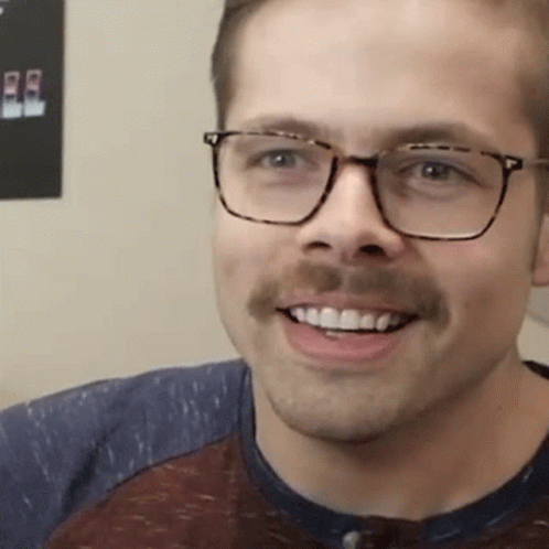 A Man With Glasses And A Mustache Is Smiling And Wearing A Shirt . GIF