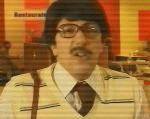 A Man With Glasses And A Mustache Is Standing In Front Of A Sign That Says Restaurante GIF