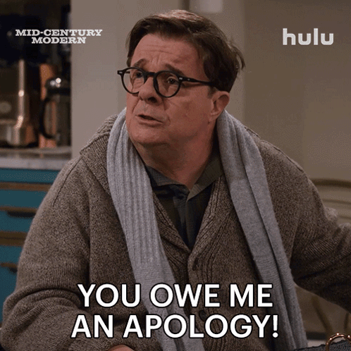 a man with glasses and a scarf around his neck says " you owe me an apology "
