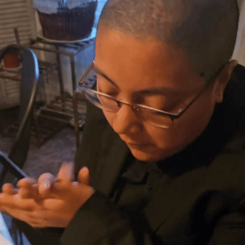 a man with glasses and a shaved head looks at his phone