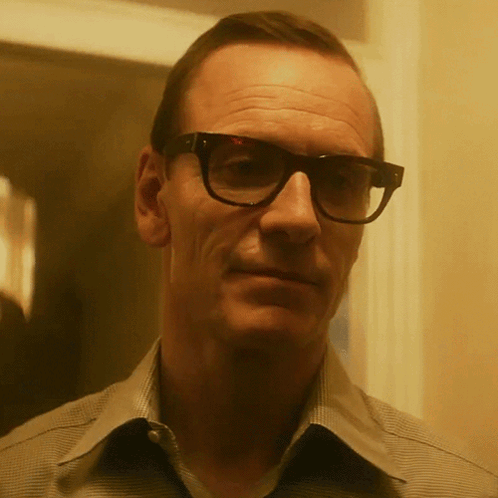 A Man With Glasses And A Striped Shirt Looks At The Camera GIF