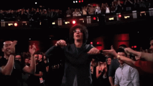 A Man With Glasses Is Dancing In Front Of A Crowd Of People GIF