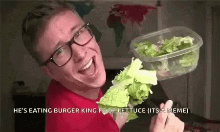 A Man With Glasses Is Holding A Container Of Lettuce And A Fork . GIF
