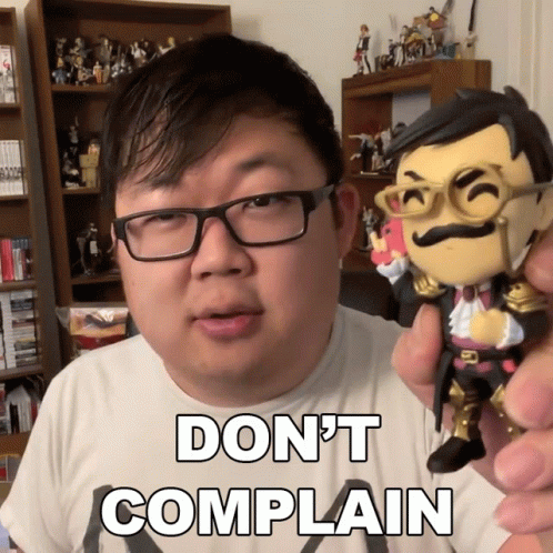 A Man With Glasses Is Holding A Figurine That Says " Do N't Complain " On It GIF