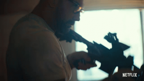 Man With Glasses Holding Gun In Front Of Window GIF