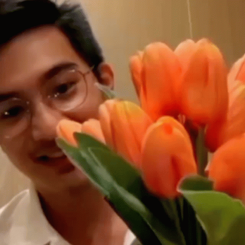 A Man With Glasses Is Looking At A Bouquet Of Orange Flowers GIF