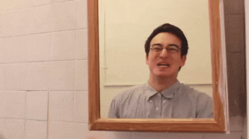 A Man With Glasses Is Looking At Himself In A Bathroom Mirror GIF