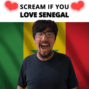a man with glasses is screaming in front of a senegal flag with the words " scream if you love senegal "