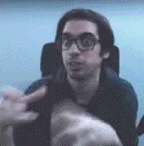 A Man With Glasses Is Sitting In A Chair And Pointing At Something GIF