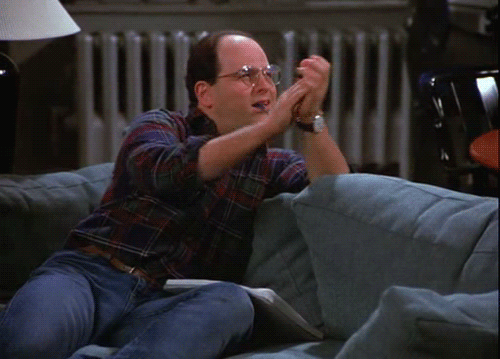 A Man With Glasses Is Sitting On A Couch With His Hands In The Air GIF