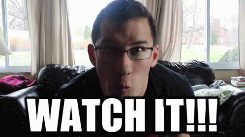 A Man With Glasses Is Sitting On A Couch With The Words Watch It GIF
