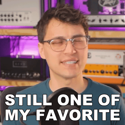 A Man With Glasses Is Smiling In Front Of A Microphone And Says " Still One Of My Favorite " GIF