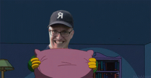 A Man With Glasses Is Smiling While Holding A Purple Pillow GIF