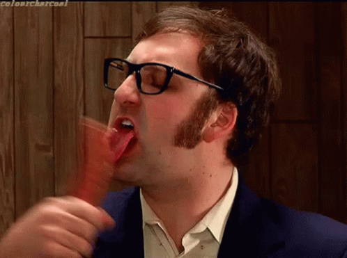 A Man With Glasses Is Sticking His Tongue Out While Eating Something GIF