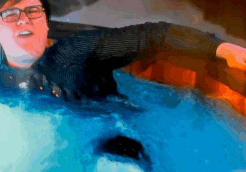 A Man With Glasses Is Swimming In A Pool Of Blue Water GIF