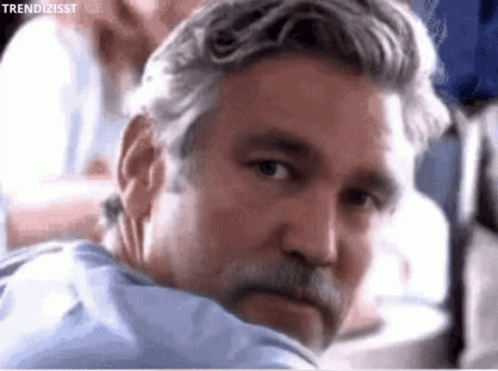 A Man With Gray Hair And A Beard Is Looking Over His Shoulder GIF