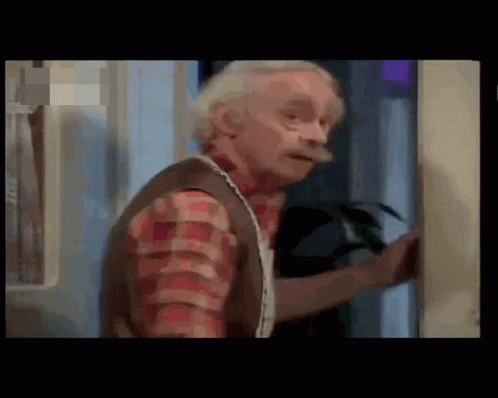 A Man With Gray Hair And A Mustache Is Standing In A Room . GIF