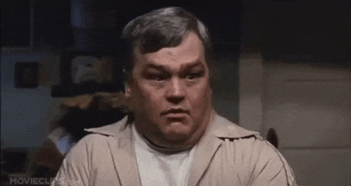 A Man With Gray Hair And A White Shirt Is Making A Face . GIF