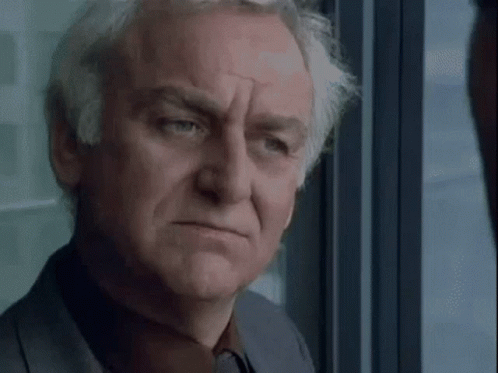 A Man With Gray Hair Is Looking Out Of A Window . GIF