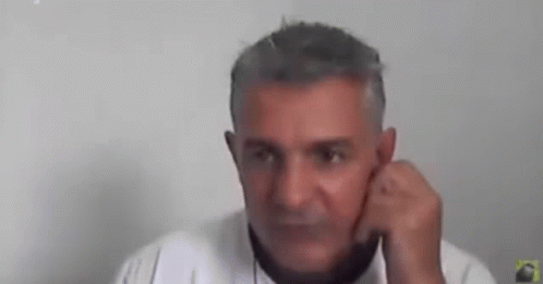 A Man With Gray Hair Is Talking On A Cell Phone While Holding His Hand To His Ear . GIF