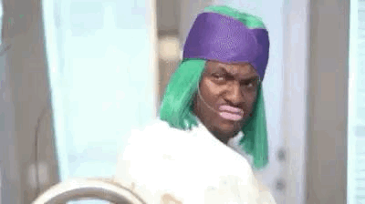 A Man With Green Hair And A Purple Headband Is Standing In Front Of A Washing Machine . GIF