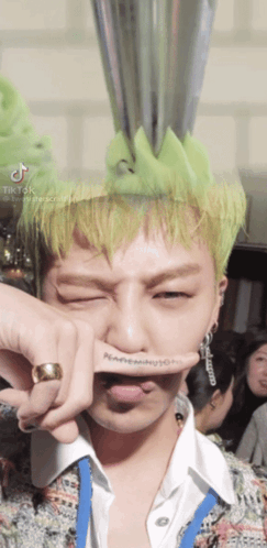 A Man With Green Hair Has A Ring On His Finger And A Tattoo On His Finger That Says Nc GIF