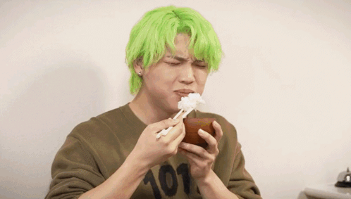A Man With Green Hair Is Eating Rice From A Bowl Next To Another Man GIF