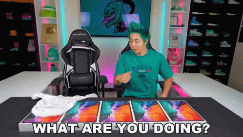 A Man With Green Hair Is Sitting In Front Of A Desk With A Chair And Says What Are You Doing GIF