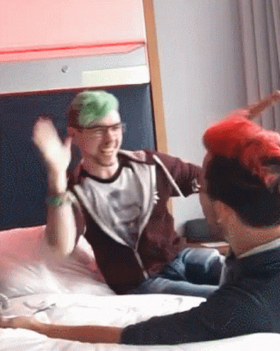 A Man With Green Hair Is Sitting On A Bed With A Man With Red Hair GIF