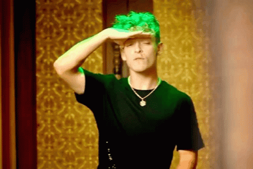A Man With Green Hair Is Wearing A Black Shirt And A Necklace And Covering His Eyes With His Hand . GIF