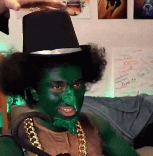 A Man With Green Paint On His Face Is Wearing A Top Hat And A Gold Chain . GIF