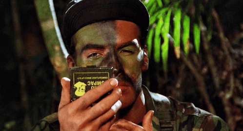 a man with half his face painted in camouflage holds a box that says jimpac