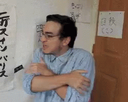 A Man With His Arms Crossed Is Standing In Front Of A Wall With Chinese Writing On It GIF