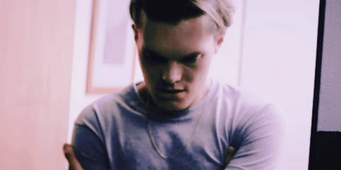 A Man With His Arms Crossed Is Wearing A Purple Shirt And A Gold Chain Around His Neck . GIF