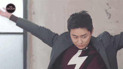 A Man With His Arms Outstretched Is Wearing A Sweater With A Lightning Bolt On It And A Suit Jacket GIF
