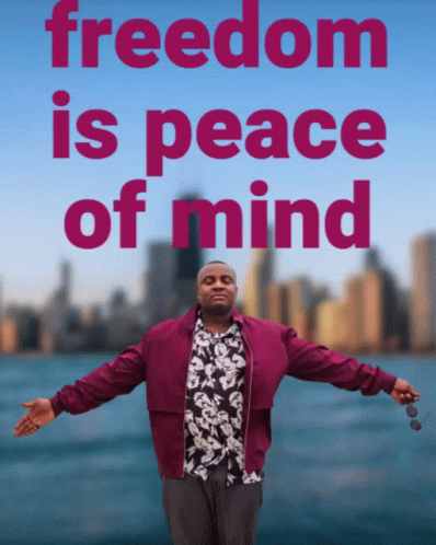 A Man With His Arms Outstretched Stands In Front Of A Sign That Says " Freedom Is Peace Of Mind " GIF