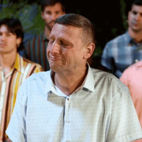 A Man With His Eyes Closed Is Standing In A Crowd Of Men GIF