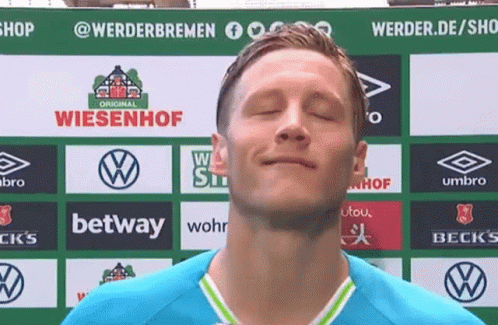 a man with his eyes closed stands in front of a sign that says ' wiesenhof ' on it