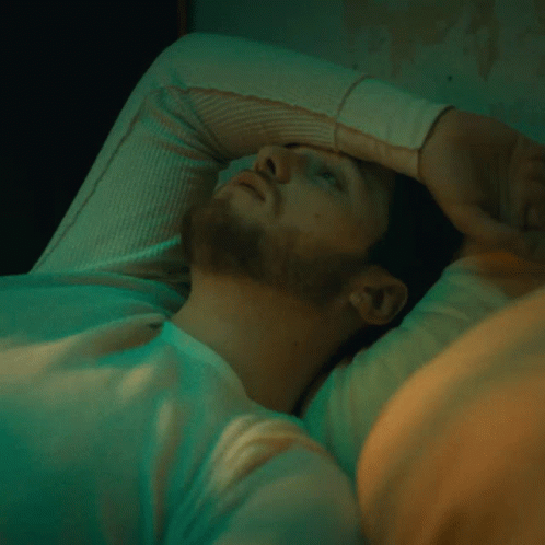 A Man With His Hand On His Forehead Is Laying In Bed GIF
