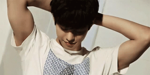 A Man With His Hands Behind His Head Is Wearing A White Fila Shirt GIF