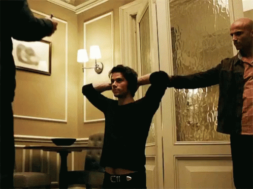 A Man With His Hands Behind His Head Stands In A Room GIF