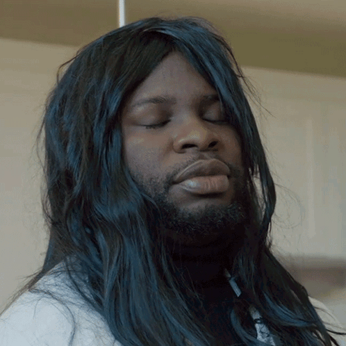 A Man With Long Black Hair And A Beard Looks Down With His Eyes Closed GIF