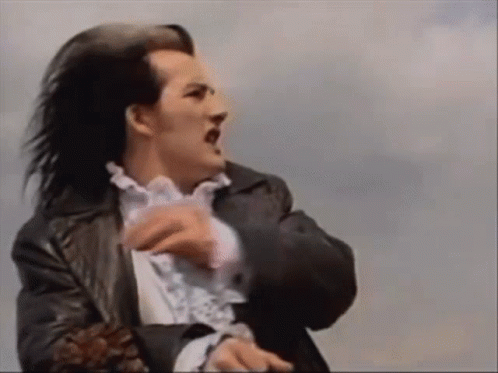 A Man With Long Black Hair Is Wearing A Black Jacket And A White Shirt . GIF