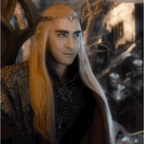 a man with long blonde hair and a crown on his head is sitting in a throne .