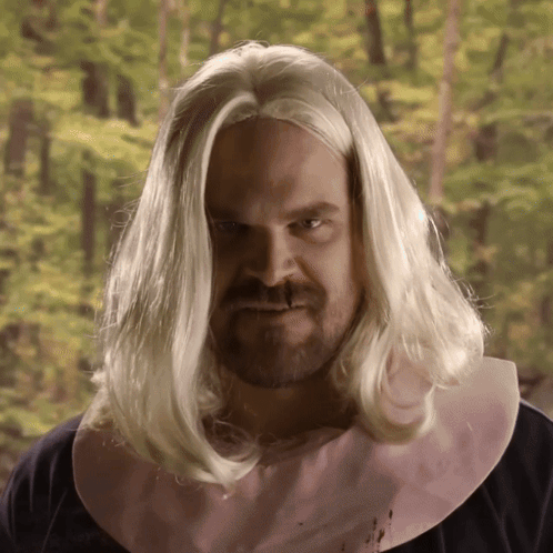 A Man With Long Blonde Hair And A Pink Bib On His Neck GIF